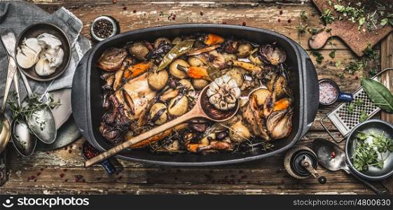 Country stew in vintage casserole with cooking spoon and roasted vegetables on rustic kitchen table background with tools , top view