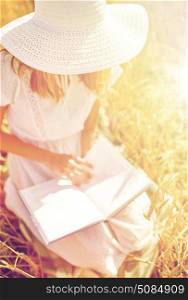 country, summer holidays, literature and people concept - close up of young woman in white straw hat and dress reading book on cereal field. close up of woman reading book on cereal field. close up of woman reading book on cereal field