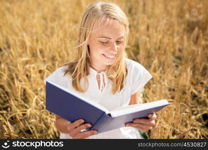 country, summer holidays, literature and people concept - smiling young woman in white dress reading book on cereal field