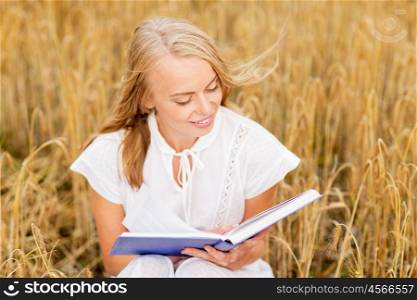 country, summer holidays, literature and people concept - smiling young woman in white dress reading book on cereal field