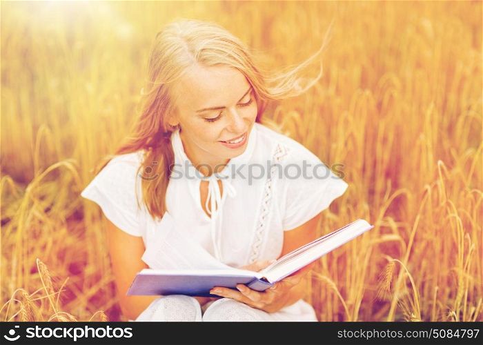 country, summer holidays, literature and people concept - smiling young woman in white dress reading book on cereal field. smiling young woman reading book on cereal field. smiling young woman reading book on cereal field