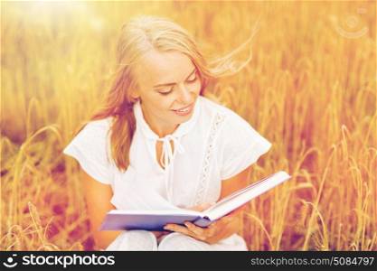 country, summer holidays, literature and people concept - smiling young woman in white dress reading book on cereal field. smiling young woman reading book on cereal field. smiling young woman reading book on cereal field
