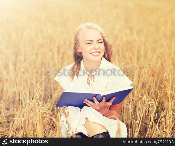 country, summer holidays, literature and people concept - smiling young woman in white dress reading book on cereal field. smiling young woman reading book on cereal field