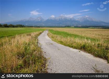 Countryside road among fields and high mountain range on the background