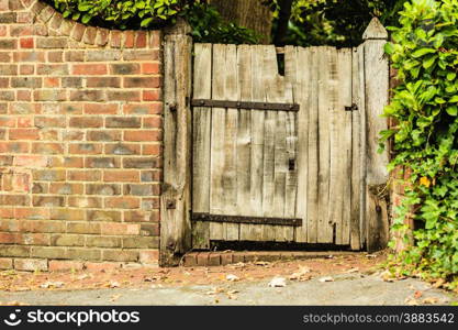 Countryside scene. Rustic old wooden gate in brick wall.