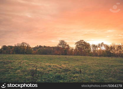 Countryside sunset with orange colors in the sky in a rural landscape with green meadows and colorful trees in the fall