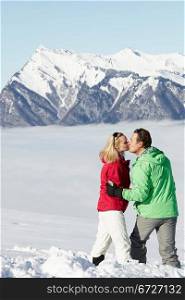 Couple Admiring Mountain View Whilst On Ski Holiday In Mountains