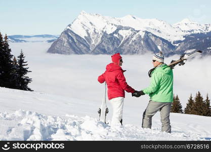 Couple Admiring Mountain View Whilst On Ski Holiday In Mountains