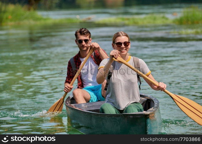 Couple adventurous explorer friends are canoeing in a wild river surrounded by the beautiful nature