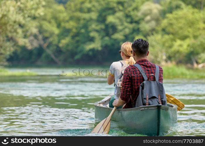 Couple adventurous explorer friends are canoeing in a wild river surrounded by the beautiful nature