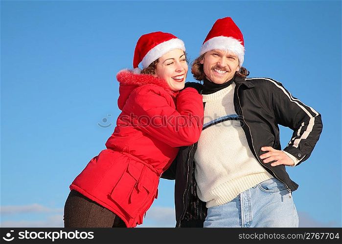 couple against blue sky background in winter in santa claus hats