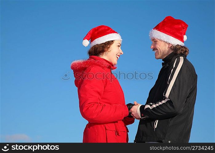 couple against blue sky background in winter in santa claus hats stand face to face