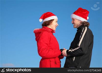 couple against blue sky background in winter in santa claus hats stand face to face