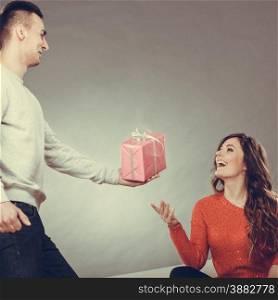 Couple and holiday concept. Handsome man surprising cheerful woman with gift box