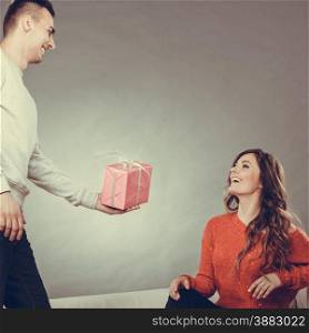 Couple and holiday concept. Handsome man surprising cheerful woman with gift box
