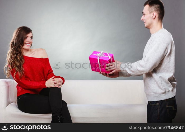 Couple and holiday concept. Handsome man surprising cheerful woman with gift box