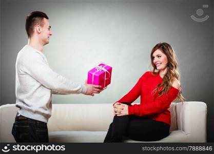 Couple and holiday concept. Smiling young man surprising cheerful woman with a gift box