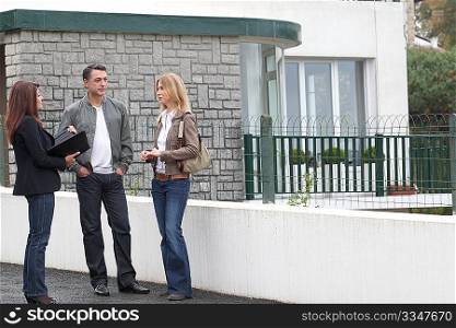Couple and real-estate agent in front of house for sale