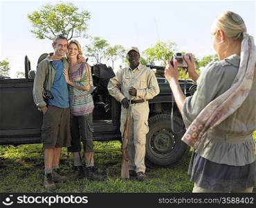 Couple and safari guide posing by jeep young woman taking photograph
