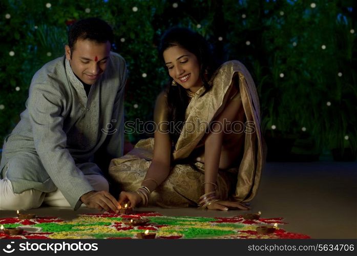 Couple arranging diyas on a rangoli