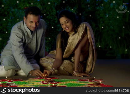 Couple arranging diyas on a rangoli
