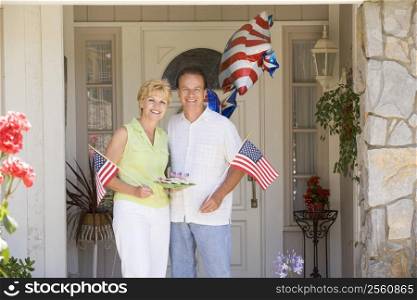 Couple at front door on fourth of July with flags and cookies smiling