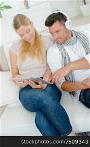 Couple at home, woman on tablet, man wearing headphones