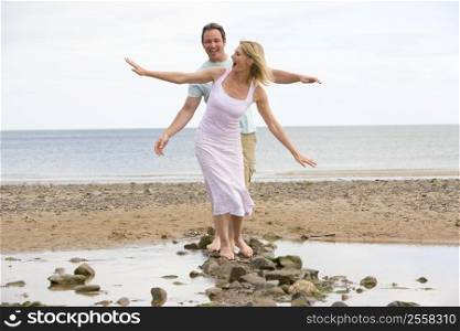 Couple at the beach walking on stones and smiling