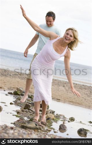 Couple at the beach walking on stones and smiling