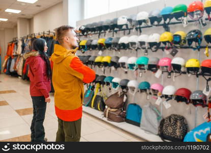 Couple at the showcase choosing helmets for ski or snowboarding, back view, sports shop. Winter season extreme lifestyle, active leisure store, customers with protect equipment. Couple choosing helmets for ski or snowboarding