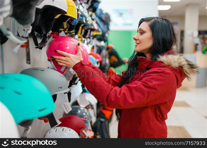 Couple at the showcase choosing helmets for ski or snowboarding, side view, shopping in sports shop. Winter season extreme lifestyle, active leisure store, customers buying protect equipment. Couple choosing helmets, shopping in sports shop