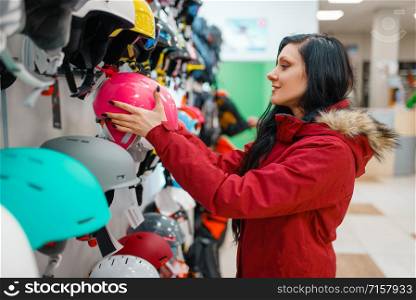 Couple at the showcase choosing helmets for ski or snowboarding, side view, shopping in sports shop. Winter season extreme lifestyle, active leisure store, customers buying protect equipment. Couple choosing helmets, shopping in sports shop