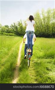 couple biking in park. Girl standing on the back of the bike