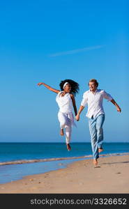 Couple - black woman and Caucasian man - walking and running down a beach in their vacation