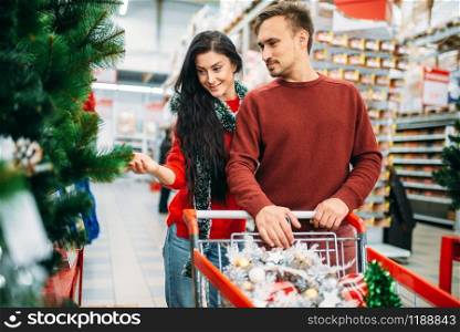 Couple buying christmas tree in supermarket. December shopping, choosing of holiday decorations. Couple buying christmas tree in supermarket