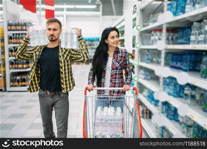 Couple buying mineral water in supermarket. Male and female customers on family shopping. Man and woman purchasing beverages