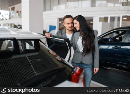 Couple buying new car in showroom. Male and female customers choosing vehicle in dealership, automobile sale, auto purchase. Couple buying new car in showroom