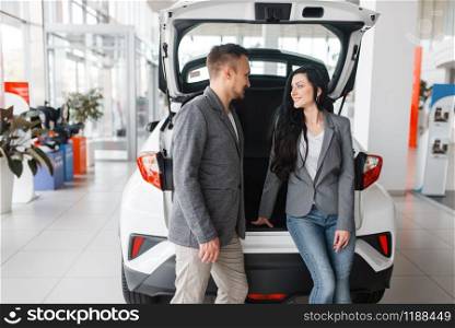 Couple buying new car in showroom, man and woman near the opened trunk. Male and female customers choosing vehicle in dealership, automobile sale, auto purchase