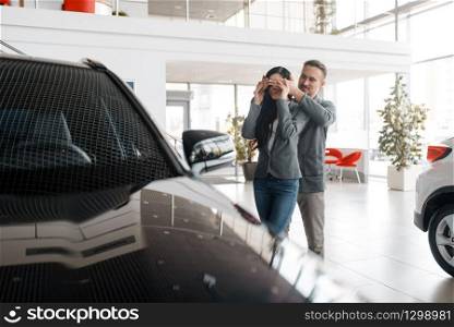 Couple buying new car in showroom, surprise for woman. Male and female customers choosing vehicle in dealership, automobile sale, auto purchase