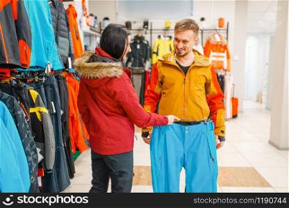 Couple buying skiing or snowboarding equipment, shopping in sports shop. Winter season extreme lifestyle, active leisure store, customer choosing ski suit