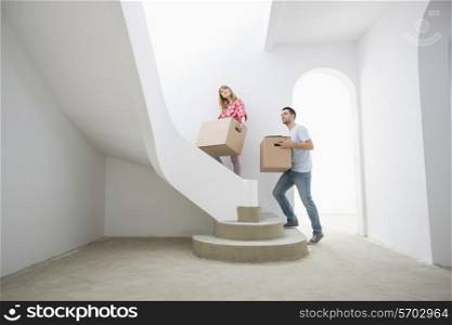 Couple carrying cardboard boxes up stairs in new house