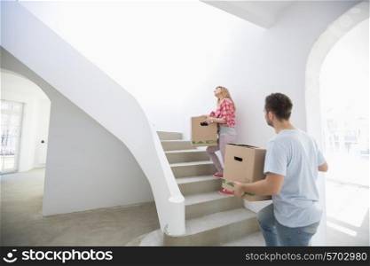 Couple carrying moving boxes up stairs in new house