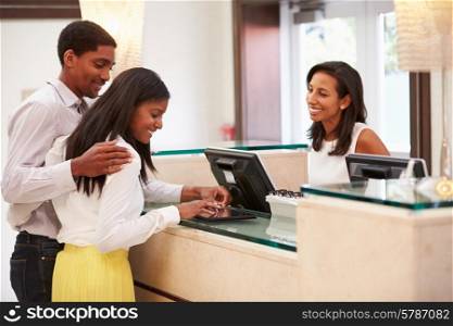 Couple Checking In At Hotel Reception Using Digital Tablet