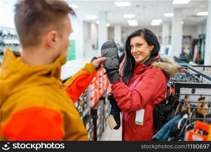 Couple choosing gloves for ski or snowboarding, sports shop. Winter season extreme lifestyle, active leisure store, customers with protect equipment. Couple choosing gloves for ski or snowboarding
