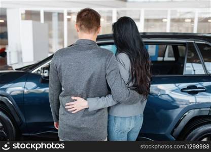Couple choosing new car in showroom, back view. Male and female customers looks vehicle in dealership, automobile sale, auto purchase