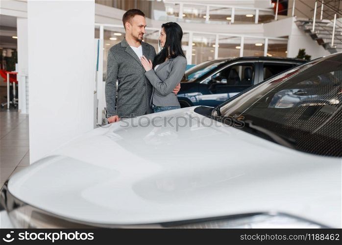 Couple choosing new car in showroom. Male and female customers looks vehicle in dealership, automobile sale, auto purchase. Couple choosing new car in showroom