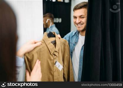 Couple choosing shirts in fitting room, family shopping in clothes store. Customers in shop, buyers in market
