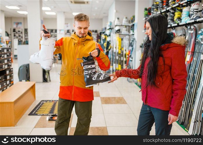Couple choosing ski or snowboarding boots, shopping in sports shop. Winter season extreme lifestyle, active leisure store, customers buying skiing equipment