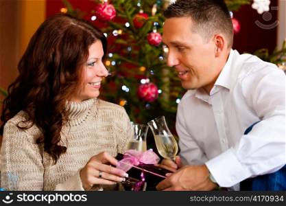Couple clinking glasses with champagne on Christmas Eve and giving gifts to each other