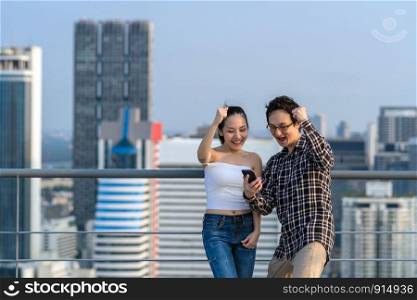 Couple colleague businessman and woman in casual suit are celebrating with the success via smart mobile phone their business on the rooftop of downtown building in business center, achievement concept